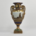 SEVRES  A GRANDEZA PARISIENSE   BELISSIMO FLOREIRO EM PORCELANA ESTILO IMPÉRIO. REMATADO EM PROFUSO OURO APLICADO SOB FUNDO EM AZUL COBALTO, ESTE LINDO FLOREIRO APRESENTA DECORAÇÃO EM RESERVA COM PRÉDIOS HISTÓRICOS PARISIENSES. REPRESENTA UMA FUSÃO CLÁSSICA DE REQUINTE ARTESANAL E ROMANTISMO HISTÓRICO.  A ELEGÂNCIA DO VASO É AINDA MAIS REALÇADA POR SUAS ALÇAS  REALÇADAS POR MASCARÕES , UM ELEMENTO DE DESIGN EMPRESTADO DA ANTIGUIDADE CLÁSSICA, E UMA FAIXA DE FOLHAS DE LOURO NA BASE QUADRADA, SIMBOLIZANDO HONRA E VITÓRIA. FRANÇA, MEADOS DO SEC. . XIX. 36 CM DE ALTURA