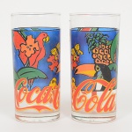VIDRO, par (2) copos cilíndricos, incolores e translúcidos, com propaganda policromada da COCA-COLA compássaros, peixes, frutas, etc., manufatura NADIR FIGUEIREDO (fundada em 1912 em São Paulo, como oficina paramáquina de escrever; em 1943 comprou a fabrica de louça Santa Rita que ficou ativa até 1950; em 1944 comprou asfazendas Santa Terezinha e Fortaleza, onde construiu uma nova fábrica chamada Vila Operária que começou a operarem 1948; em 1947 iniciou a produção do copo de vidro americano; em 1955 iniciou a produção de copo para envase derequeijão; registrou as seguintes marcas: em 1956 a KOPAL; em 1957 a ROSICLER e PIREFRAX; em 1979 aKERAMIK; em 1982 a POTTERY; em 1992 a DURAMIK; em 1993 encerrou a produção de louça), medindo 14 cmaltura e 6,5 cm diâmetro, ideais para coleção de cristaleira ou bar, vide foto.