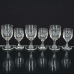 VIDRO, seis (6) taças de pé alto, incolores e translúcidas, dois tamanhos distintos: 3 para licor, bojo lapidado emsulcos e estrelas, fuste cilíndrico, base em bolacha, medindo 7,5 cm altura; 3 para vinho do porto na mesmapadronização, medindo 8,5 cm altura, todas com sinais de uso, vide foto.