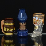 VIDRO, três (3) itens miniatura: 1 caneca na forma de bota, souvenir de Frankfurt, Alemanha, selo da E & ABockling Neudenau, medindo 7,5 cm altura; 1 caneca, souvenir da Flórida, USA, tonalidade âmbar, translúcida, alça emmadeira fixada por fita metálica, medindo 6 cm altura; 1 miniatura representando lamparina, tonalidade azul translúcida,monture em folha de flandres com sinais de oxidação, medindo 9,5 cm altura, vide foto.