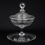 CRISTAL FRANCÊS, uma (1) compoteira de pé alto com tampa e presentoir, incolor e translúcida, lapidada combarrado em elementos vegetalistas, pega da tampa facetada quase esférica, fuste no formato de balaustre, base embolacha, presentoir com bicados na borda, medindo 24 cm altura, sinais de uso, vide foto, possivelmente manufatura daCRISTALERIE ROYALE DE SAINT LOUIS (fundada em 1586 no vale de Munzthal em Mosela como VerrerieMunzthal; encerrou as atividades em meados do século XVII devido a devastação causada na região pela Guerra dos 30Anos; em 1767 através de Carta Patente concedida pelo Rei Louis XV, retornou as atividades e passou a se chamarVerrerie Royale de Saint Louis; em 1781 M. de Beaufort, descobre a composição do cristal, na época apenas a Inglaterradominava a técnica do cristal de chumbo, assim a fabrica passou a se chamar Cristallerie Royale de Saint Louis; noséculo XIX foi a era de ouro da fábrica com várias introduções: em 1830 o cristal moldado; em 1834 criou o serviçoTrianon; em 1837 introduziu a cor; em 1845 a filigrana, a opalina, o cristal duplo (overlay) e o triplo (double overlay);em 1867 a gravura acidada; em 1989 a Hèrmes comprou a participação acionária da fábrica).