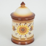 CERÂMICA, um (1) pote com tampa, ornamentação floral pintada a mão, degrade nas tonalidades marrom eamarelo sobre fundo branco, medindo 21 cm altura, sinais de uso, vide foto.