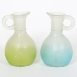 VIDRO, par (2) galhetas sem as tampas, moldadas com singelos elementos vegetalistas, ambas em degrade eacetinadas, uma em azul e incolor, outra em verde e incolor, ambas com bicados na borda, medindo 11,5 cm altura,sinais de uso, vide foto.