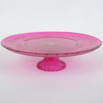 VIDRO,um (1) prato para bolo de pé alto, translúcido, esmaltação na tonalidade lilás, modelado em geométricos,perolados e elementos vegetalistas, base canelada, medindo 32,5 cm diâmetro e 9,5 cm altura, sinais de uso, vide foto.