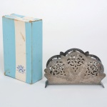 METAL PRATEADO, um (1) porta guardanapo vazado em elementos vegetalistas, marca ÁUREA-PRATA 90, acondicionado na embalagem original em papel cartonado, não aparenta ter sido usado, ideal para presente, medindo 12,5 cm comprimento, vide foto.