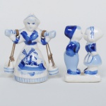 PORCELANA, dois (2) souvenires holandeses, pintados a mão na técnica blue and white, figurativos, representando casal se beijando e mulher carregando baldes (quebrada e colada), medindo a maior peça 7 cm altura, origem Delf, vide foto.