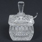 CRISTAL E VIDRO, uma (1) molheira quadrangular com tampa, incolor e translúcida, moldada em geométricos e bico de jaca, fundo estrelado, concha adaptada, medindo 13 cm altura, possui bicados em uma das quinas, sinais de uso, vide foto.