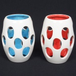 FAIANÇA OU CERÂMICA, par (2) adornos vazados ou mangas para luminária, pintadas nas tonalidades branca e vermelha em uma e branca e azul em outra, sem marca de manufatura aparente, formato de barrica, medindo 14 cm altura, sinais de uso, vide foto.