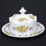 PORCELANA, uma (1) queijeira com presentoir, ornamentação policromada com flores e frutos, arremates a ouro, medindo 25,5 cm diâmetro, desgastes na douração, manufatura GERMER (fundada em 1950 em Timbó, SC, como fabricante de acessórios para maquinário têxtil; em 1964 passou a produzir componentes para lançadeiras; em 1969 passou a produzir isoladores elétricos; em 1978 quando assumiu o controle da POLOVI Campo Largo, PR passou a produzir porcelana de mesa; em 1988 modernizou a fabrica com a aquisição de novos fornos, atualmente é a segunda maior produtora de porcelana do Brasil), sinais de uso, vide foto.