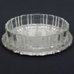 VIDRO E AÇO INOX, dois (2) itens: 1 fruteira, incolor e translúcida, modelagem geometrizada, medindo 18 cm diâmetro e 5 cm altura, acompanha presentoir com borda relevada em volutas, sem marca de manufatura aparente, confecção mecanizada na técnica de estamparia, medindo 20 cm diâmetro, ambos com sinais de uso, vide foto.