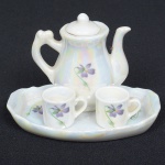 PORCELANA, conjunto tete a tete miniatura com quatro (4) itens: 1 bandeja; 1 bule e 2 canecas, fundo nacarado, singela ornamentação floral policromada, sem marca de manufatura aparente, medindo a maior peça 10 x 7 cm, ideal para coleção de cristaleira, vide foto.