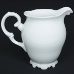 PORCELANA, uma (1) jarra bojuda, tonalidade branca, alça sinuosa, pés recortados, manufatura SCHMIDT (Pomerode, SC; Mauá, SP; Campo Largo, PR, fundada em 1945, ainda em atividade, maior fábrica de porcelana da América Latina), medindo 16 cm altura, sinais de uso, vide foto.