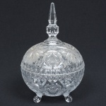 CRISTAL uma (1) compoteira no padrão dito bilha, incolor e translúcidas, lapidação vegetalista e geometrizada, pega da tampa lembra um minarete, base trípode terminando em volutas, detalhes acetinados, medindo 24 cm altura, sinais de uso, vide foto.