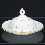 PORCELANA PORTUGUESA, uma (1) manteigueira com tampa e presentoir acoplado, ornamentação floral policromada, arremates a ouro, manufatura VISTA ALEGRE (fundada em 1824, pelo negociante, lavrador, industrial e político, José Ferreira Pinto Basto, através de alvará concedido por D. João VI, tendo seu fundador associado a fábrica os seus 15 filhos, ficando a sociedade denominada Ferreira Pinto & Filhos; cinco anos mais tarde recebe o título real pelo reconhecimento de sua arte e sucesso, ficando conhecida como Real Fábrica da Vista Alegre, começou no fabrico de vidros enquanto se empenhava em esforços para a produção de porcelana, os primeiros ensaios conseguidos foram imperfeitos denominado loiça de pó de pedra, através de boas relações com a fábrica francesa de Sevres conseguiu as receitas para o fabrico de porcelana, somente em 1832, por sorte, é encontrado um jazigo de caulim situado em Aveiro, próximo a Ílhavo, a partir desta data o fabrico de porcelana foi se aperfeiçoando em Portugal, 1851 expôs com sucesso no Palácio de Cristal em Londres; 1852 D. Fernando II visita a fábrica e encomenda uma baixela completa; 1867 recebeu sua primeira premiação na Exposição Universal de Paris; 1880 interrompe a produção de vidros para se dedicar exclusivamente a porcelana; 1964 inauguração do Museu Histórico da Vista Alegre; ainda em funcionamento), medindo 18 cm diâmetro, ideal para coleção de cristaleira, vide foto.