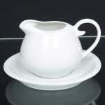 PORCELANA, uma (1) cremeira com pires, tonalidade branca, sem marca de manufatura aparente, medindo a maior peça 14,5 cm diâmetro, sinais de uso, vide foto.