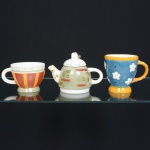 FAIANÇA, três (3) itens policromados, pintados a mão: 1 bule com tampa, detalhes vegetalistas e legenda, medindo 12 cm altura; 2 canecas distintas, relevadas em flores e frisos, medindo 11 cm diâmetro e 8,5 cm altura; 10,5 cm diâmetro e 11 cm altura, todos os itens com sinais de uso, vide foto.