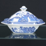 FAIANÇA INGLESA, uma (1) terrina com tampa, quadrangular, ornamentação dita WILLON (Segundo a lenda chinesa: Um certo Mandarim tinha uma leal e devotada filha, possuidora de rara beleza. Certo dia, em que descobre que ela estava apaixonada por um carteiro que lhe fazia a corte, e que era por ela correspondida, expulsa a filha de casa e roga-lhe uma praga: que ao ser trocado o primeiro beijo pelo casal, eles se transformariam em dois pombos), também conhecida como pombinhos, manufatura WOOD & SONS Ltd. (fundada em 1865, funcionou na Potteries New Wharf em Trent e mais tarde na Pottery Stanley em Burlem, fechou em 2005), tonalidade azul sobre fundo branco, medindo 24 x 24 x 15 cm, possui o craquelê característico do envelhecimento de toda a faiança, sinais de uso, vide foto.