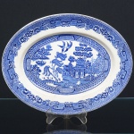 FAIANÇA INGLESA, uma (1) travessa oval, ornamentação dita WILLON (Segundo a lenda chinesa: Um certo Mandarim tinha uma leal e devotada filha, possuidora de rara beleza. Certo dia, em que descobre que ela estava apaixonada por um carteiro que lhe fazia a corte, e que era por ela correspondida, expulsa a filha de casa e roga-lhe uma praga: que ao ser trocado o primeiro beijo pelo casal, eles se transformariam em dois pombos), também conhecida como pombinhos, manufatura WOOD & SONS Ltd. (fundada em 1865, funcionou na Potteries New Wharf em Trent e mais tarde na Pottery Stanley em Burlem, fechou em 2005), tonalidade azul sobre fundo branco, medindo 31 x 24 cm, raspados na borda visto pelo verso, possui o craquelê característico do envelhecimento de toda a faiança, sinais de uso, vide foto.
