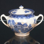 FAIANÇA INGLESA, um (1) açucareiro com tampa, ornamentação dita WILLON (Segundo a lenda chinesa: Um certo Mandarim tinha uma leal e devotada filha, possuidora de rara beleza. Certo dia, em que descobre que ela estava apaixonada por um carteiro que lhe fazia a corte, e que era por ela correspondida, expulsa a filha de casa e roga-lhe uma praga: que ao ser trocado o primeiro beijo pelo casal, eles se transformariam em dois pombos), também conhecida como pombinhos, manufatura WOOD & SONS Ltd. (fundada em 1865, funcionou na Potteries New Wharf em Trent e mais tarde na Pottery Stanley em Burlem, fechou em 2005), tonalidade azul sobre fundo branco, medindo 12 cm de altura e diâmetro mais as alças, possui o craquelê característico do envelhecimento de toda a faiança, além de manchas, sinais de uso, vide foto.