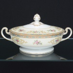 PORCELANA JAPONESA, uma (1) terrina com tampa, pega modelada em flor, alças sinuosas, ornamentação floral policromada, borda com faixa na tonalidade azul claro e elementos vegetalistas em policromia, arremates a ouro, manufatura NORITAKE (1858 - Japão assinou o Tratado de Amizade e Comércio com os EUA, Holanda, Rússia, Reino Unido e França; 1867 fim do Shogunato e início da era Meiji; 1876 - Morimura-Kumi formada em Tóquio para exportação Os Morimuras & The Okuras unidos, a Companhia Hinode se estabelece na cidade de Nova York para o varejo; 1879 - A Companhia Hinode fecha. Morimura Bros & Co., se estabelece em Nova York; 1880 - Hiroses juntou-se a Morimura-Kumi em Tóquio; 1882 - Morimura Bros & Co., decidiu ser o atacadista; 1884 Morimura-Kumi subcontrata atelieres de decoração em porcelana nas cidades de Tokyo, Nagoya e Kyoto; 1918 - Morimura-Kumi é reorganizada como Morimura Bros, Inc.; 1921 - Morimura Bros de New York é incorporada a Morimura Bros, Inc. De Tokyo; 1947 - Noritake Co., Inc. com sede em Nova York; 1981 - Nome japonês da Companhia alterado para Noritake Co. Limited), modelo COLBY, medindo 22,5 cm diâmetro mais as alças e 15 cm altura, sinais de uso, vide foto.