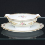 PORCELANA JAPONESA, uma (1) molheira com presentoir acoplado, ornamentação floral policromada, borda com faixa na tonalidade azul claro e elementos vegetalistas em policromia, arremates a ouro, manufatura NORITAKE (1858 - Japão assinou o Tratado de Amizade e Comércio com os EUA, Holanda, Rússia, Reino Unido e França; 1867 fim do Shogunato e início da era Meiji; 1876 - Morimura-Kumi formada em Tóquio para exportação Os Morimuras & The Okuras unidos, a Companhia Hinode se estabelece na cidade de Nova York para o varejo; 1879 - A Companhia Hinode fecha. Morimura Bros & Co., se estabelece em Nova York; 1880 - Hiroses juntou-se a Morimura-Kumi em Tóquio; 1882 - Morimura Bros & Co., decidiu ser o atacadista; 1884 Morimura-Kumi subcontrata atelieres de decoração em porcelana nas cidades de Tokyo, Nagoya e Kyoto; 1918 - Morimura-Kumi é reorganizada como Morimura Bros, Inc.; 1921 - Morimura Bros de New York é incorporada a Morimura Bros, Inc. De Tokyo; 1947 - Noritake Co., Inc. com sede em Nova York; 1981 - Nome japonês da Companhia alterado para Noritake Co. Limited), modelo COLBY, medindo 23,5 x 15,5 x 8 cm, sinais de uso, vide foto.