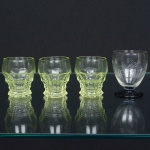 VIDRO, quatro (4) taças para licor de dois modelos distintos: 3 na tonalidade verde, translúcidas, modelagem geometrizada, medindo 5 cm altura; 1 com bojo obcônico, incolor e translucida, singela lapidação, base em bolacha na tonalidade azul translúcida, medindo 6 cm, todas com sinais de uso, vide foto.