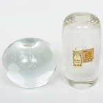 VIDRO, dois (2) pesos de tamanhos distintos, incolores e translúcidos, possuem bulicados internos, um deles com selo da CA DORO CRISTAIS, medindo o maior 9,5 cm altura, vide foto.