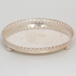 METAL PRATEADO, uma (1) pequena salva circular, lisa, borda vazada e intercalada por círculos, pés com terminações em bolacha, sem marca de manufatura aparente, medindo 15 cm diâmetro, sinais de uso, vide foto.