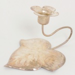 METAL PRATEADO, uma (1) palmatória com base e bobeche no formato de folha e flor, alça sinuosa, sem marca de manufatura aparente, medindo 10,5 cm comprimento, sinais de uso, vide foto.