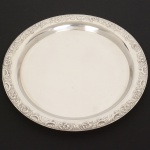 METAL PRATEADO OU AÇO INOX, uma (1) bandeja circular, confecção mecanizada na técnica de estamparia, borda relevada em volutas e elementos vegetalistas, medindo 31 cm diâmetro, sinais de uso, vide foto.