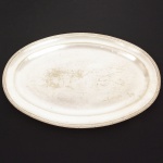 METAL PRATEADO, uma (1) imponente travessa oval, borda reforçada e relevada no padrão Império Napoleônico com frisos intercalados por X, manufatura WOLFF (tradição desde 1894), medindo 70,5 x 46 cm, sinais de uso, vide foto.