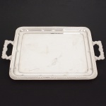 AÇO INOX, uma (1) bandeja retangular, confecção mecanizada na técnica de estamparia, borda plissada e com relevo geometrizado, alças idem, sem marca de manufatura aparente, medindo 43 x 33 cm mais as alças, sinais de uso, vide foto.