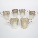 METAL PRATEADO, seis (6) suportes para copo, obcônicos, borda recortada e vazada em elementos vegetalistas estilizados, alça relevada em texturização e elementos vegetalistas, medindo 8 cm altura e 7,5 cm diâmetro, sem marca de manufatura aparente, sinais de uso, vide foto.