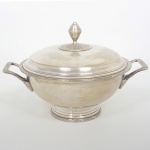 METAL PRATEADO, uma (1) terrina com tampa, ornamentação no padrão Império Napoleônico, borda e base reforçadas, relevadas em frisos intercalados por X, alças na mesma padronização, além de laçarotes e elementos vegetalistas, pega da tampa na forma de pinha, medindo 26 cm diâmetro mais as alças, manufatura WOLFF (tradição desde 1894), sinais de uso, vide foto.