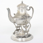 METAL PRATEADO, um (1) antigo samovar, bule ornado em caneluras, alça relevada em volutas e elementos vegetalistas, base vazada em elementos vegetalistas, possui queimador, sem marca de manufatura aparente, medindo 29 cm altura, sinais de uso, vide foto.