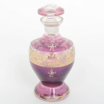 VIDRO VENEZIANO, uma (1) licoreira, incolor e translúcida, esmaltada em roxo com flores em policromia, resquícios de douração, medindo 20 cm altura, sinais de uso, vide foto.