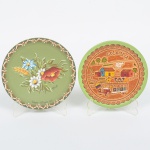 DIVERSOS, dois (2) pratos souvenires confeccionados em madeira torneada: 1 com aplique em couro, pintado em policromia, retratando cena do cotidiano rural, origem Colômbia; 1 pintado a mão com flores em policromia e assinado C. GRATT, origem Treze Tilias  SC, medindo respectivamente 14,5 cm e 15,5 cm, vide foto.