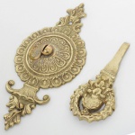 BRONZE, dois (2) itens: 1 adorno para fixação em parede, relevado em elementos vegetalistas, possui dois ganchos adaptados, medindo 22,5 cm; 1 parte de objeto, possivelmente de um cabo, relevado em concha e elementos vegetalistas, medindo 13,5 cm comprimento, ambos com sinais de uso, vide foto.