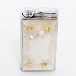 COLECIONISMO, um (1) isqueiro em metal prateado, ornado com placa em madrepérola, entalhes vegetalistas e cravações de pedras com facetado 8 x 8, marca NACON  CORONA MFG. Co., medindo 5,5 x 3 x 1 cm, vide foto.