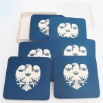 DIVERSOS, três (3) porta copos ornados com brasão de armas representado por águia e três coroas, lito sobre cortiça, acondicionados na caixa e sem uso, medindo 10,5 x 10,5 cm, ideais para presente, vide foto.