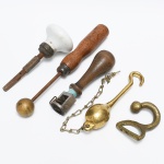 DIVERSOS, cinco (5) itens: 1 antiga maçaneta confeccionada em louça; 1 boleadora para confecção de artesanato; 1 carimbo datador de antiga loja de ferragens; 2 ganchos em bronze, todos os itens com sinais de uso, vide foto.