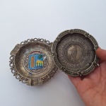 Dupla com 1 CINZEIRO e 1 PRATINHO de metal com ilustrações em relevo. Peças decorativas no estado das fotos, sem testes de funcionamento.