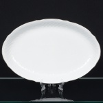 Porcelana Beatriz, Natal - RN. Elegante travessa oval em porcelana nacional, esmaltagem vítrea na cor branca, decoração na técnica "bianco sopra bianco", com padrão floral e 'lattice' em reserva relevados na prória pasta, distribuídos ao redor da orla, borda recortada e contornada por friso prateado. Marca da manufatura no verso. Medida: Comp.: 37,5 x Larg.: 25 cm.