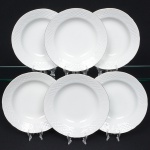 Porcelana Beatriz, Natal - RN. Elegante conjunto de pratos rasos em porcelana nacional, esmaltagem vítrea na cor branca, decoração na técnica "bianco sopra bianco", com padrão floral e 'lattice' em reserva relevados na prória pasta, distribuídos ao redor da orla, borda recortada e contornada por friso prateado. Marca da manufatura no verso. Composto de seis(06) unidades. Medida: Diam.: 20
