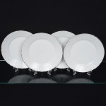 Porcelana Beatriz, Natal - RN. Elegante conjunto de pratos rasos em porcelana nacional, esmaltagem vítrea na cor branca, decoração na técnica "bianco sopra bianco", com padrão floral e 'lattice' em reserva relevados na prória pasta, distribuídos ao redor da orla, borda recortada e contornada por friso prateado. Marca da manufatura no verso. Composto de quatro04) unidades. Medida: Diam.: 24 cm.
