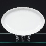 Porcelana Beatriz, Natal - RN. Elegante travessa oval em porcelana nacional, esmaltagem vítrea na cor branca, decoração na técnica "bianco sopra bianco", com padrão floral e 'lattice' em reserva relevados na prória pasta, distribuídos ao redor da orla, borda recortada e contornada por friso prateado. Marca da manufatura no verso. Medida: Comp.: 31 x Larg.: 21 cm.