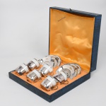 WOLFF  / Porcelana Real, Mauá - SP(Fundada em 1943 por Fritz Erwin Schmidt).  Conjunto de xícaras para café com recipiente em porcelana nacional, esmaltação branca, borda circundada por friso prateado, suporte e pires confeccionados em metal espessurado à prata, formato cilíndrico com alça lateral em voluta. Respectivas marcas de manufatura ao fundo. Composto de seis(06) unidades. Sem uso, acondicionadas em caixa original. Medidas: Xícara Alt.: 5 x Comp.: 7 x Larg.: 4,5 cm; Pires: Diam.: 10,5 cm.