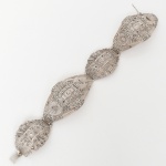 Pulseira composta por elos articulados em prata, estruturados em módulos vazados de contorno losangular e ovalado, intercalados por elementos centrais em formato geométrico. Conjunto concebido segundo a linguagem formal do estilo Art Déco, com composição simétrica, organização axial e predominância de linhas retas e escalonadas.Superfície integralmente trabalhada com cravação de marcassitas em engaste de grão, dispostas em composição geométrica e radial, elos unidos por articulações metálicas ocultas, proporcionando flexibilidade ao conjunto, fecho integrado ao último módulo, com sistema de lingueta e trava de segurança. Verso com estrutura vazada e reforços estruturais internos. Presença de punção indicativa da prata do toque 0,925. Peso: 46 gramas. Medidas: Alt.: 3 x Comp.: 18,5 cm.