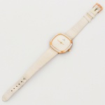 Relógio de pulso feminino, fabricação suíça, caixa de formato quadrangular de cantos arredondados, aro externo em metal dourado e corpo em material sintético branco. Mostrador liso em tonalidade branca, inscrição NATAN sob a posição das 12 horas e indicação SWISS MADE na posição das 6 horas. Ponteiros centrais para horas e minutos. Coroa lateral canelada. Tampa posterior em aço inoxidável, gravada FOND ACIER INOXYDABLE e numerada 217933. Movimento de fabricação suíça. Pulseira em couro sintético de tonalidade branca, fixada por barras metálicas, com passadores e fecho tipo fivela em metal dourado. Medidas: Caixa: Diam.: 3 cm. Pulseira aberta: 19, cm. Apresenta marcas de uso e do tempo, vide foto. Não está funcionando.