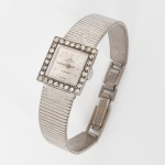 Relógio de pulso feminino com caixa de formato quadrangular, mostrador prateado com acabamento radial, marcadores lineares aplicados e ponteiros centrais para horas e minutos. Inscrições BUCHERER, 17 JEWELS e SWISS no mostrador. Aro frontal guarnecido por fileira perimetral de gemas incolores lapidadas em corte brilhante, cravadas em garras. Caixa metálica com fundo liso numerado 51996. Coroa lateral gravada com inicial B. Movimento mecânico de corda manual, 17 rubis. Pulseira metálica articulada com fecho integrado. Não está funcionando. Apresenta sinais de oxidação, marcas de uso e do tempo, visíveis nas fotografias. Medidas: Caixa:  Alt.: 2 x Comp.: 2 cm. Pulseira aberta: Comp.: 15 cm.